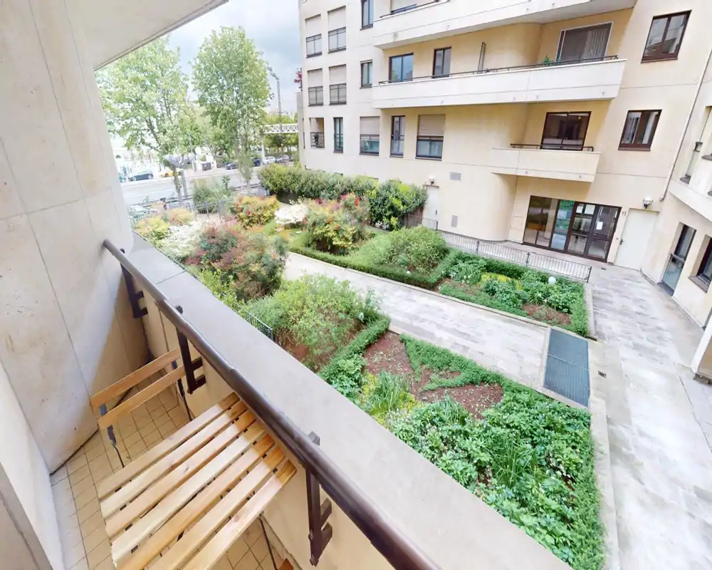 Sunny private balcony overlooking a landscaped internal courtyard, with a compact wooden foldable bench — ideal for morning coffee and city views.