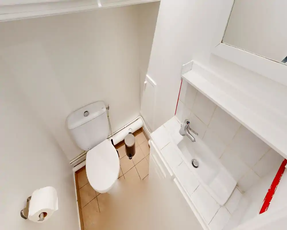 Compact bathroom with a toilet, small sink and mirror; clean white tiles and simple fittings ideal for a guest WC.