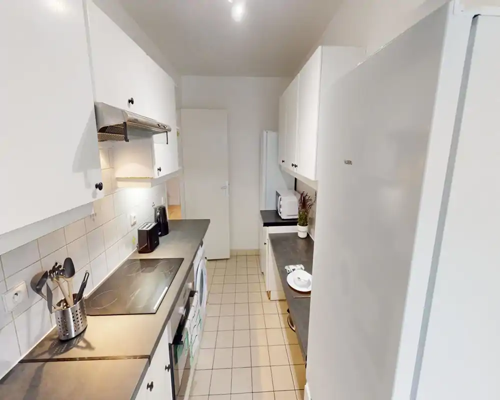Bright, modern galley kitchen with white cabinets, ceramic tile floor and a glass-ceramic hob. Clean countertops, toaster, microwave and a fridge provide functional appliances for short or long stays.