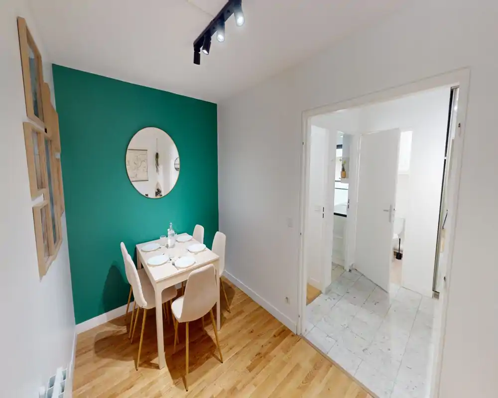 Bright, modern dining area with a small table set for four, accent teal wall and round mirror for a cozy atmosphere.