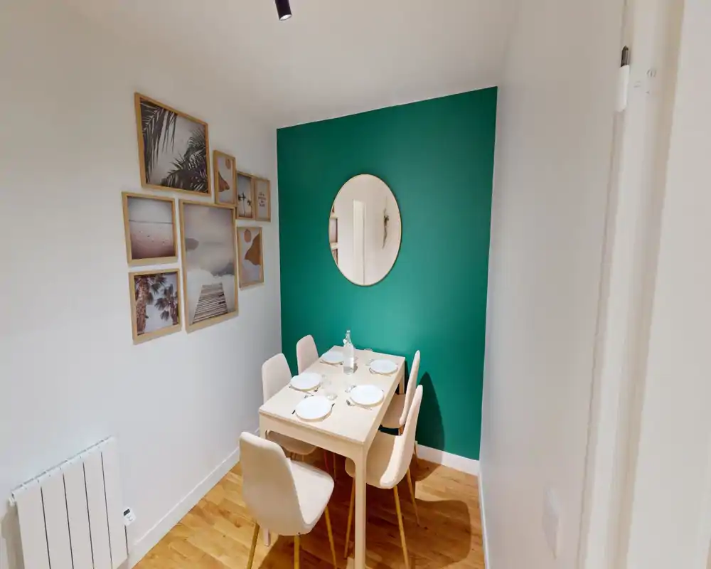 Cozy, modern dining nook with a small wooden table set for four, soft upholstered chairs, a decorative round mirror and gallery wall against a green accent wall.