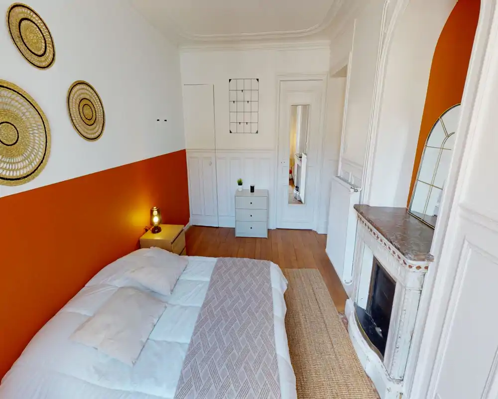 Chambre lumineuse et soignée avec un grand lit double, mur d'accent terracotta, décorations murales et une cheminée ancienne — chaleureuse et bien éclairée pour une annonce.