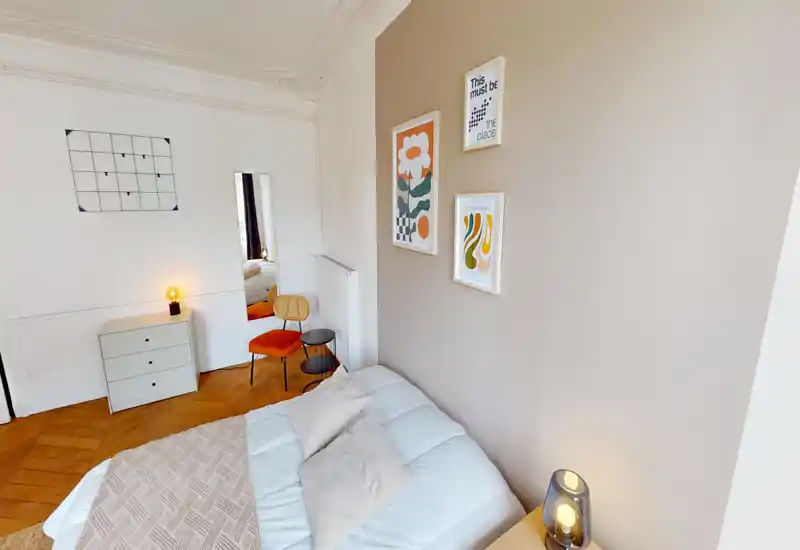 Bright, styled bedroom with a comfortable double bed, soft pillows and warm decorative accents including a bedside lamp and framed prints.