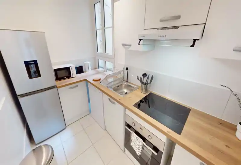 Compact modern kitchen with a wooden countertop, induction hob, built-in oven and refrigerator. Bright, clean design with useful appliances (microwave, kettle) and organized utensils.