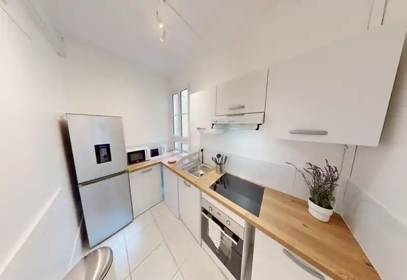 Compact modern kitchen with white cabinets, wooden countertops, built-in oven and induction hob, fridge and small appliances — bright and well organized.