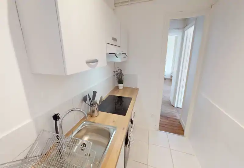 Compact modern galley kitchen with a wooden countertop, stainless sink, induction hob and white cabinets — bright, clean and efficiently arranged.