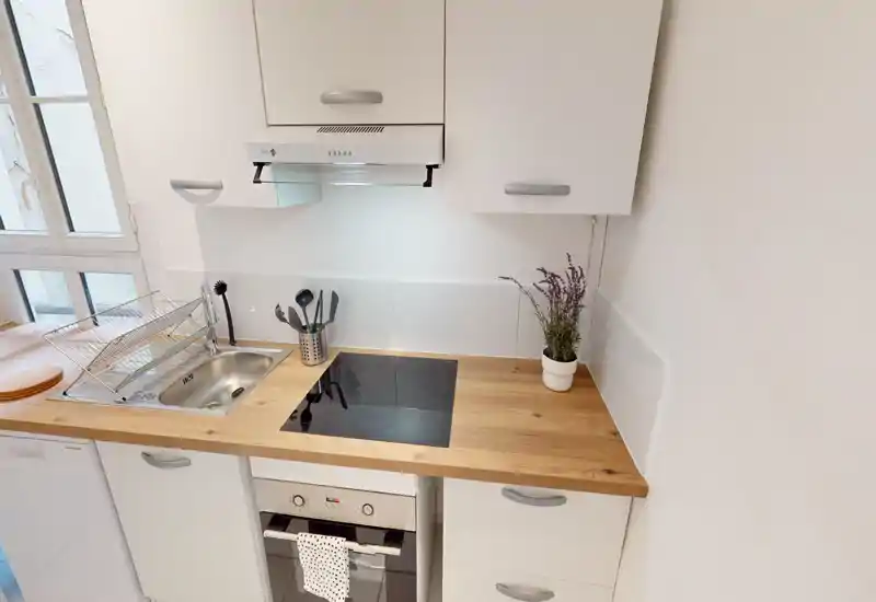 Compact modern kitchen with a wooden countertop, induction hob, sink and clean white cabinets — bright and neatly arranged for efficient cooking.