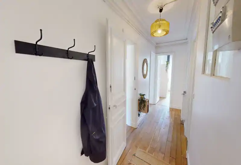 Bright, narrow entrance hallway with wooden floors, wall hooks and a woven pendant light — clean, welcoming circulation space leading into the home.
