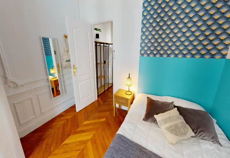 Chambre lumineuse et élégante avec mur accent turquoise, papier peint à motifs, parquet et un lit douillet avec coussins et lampe de chevet.