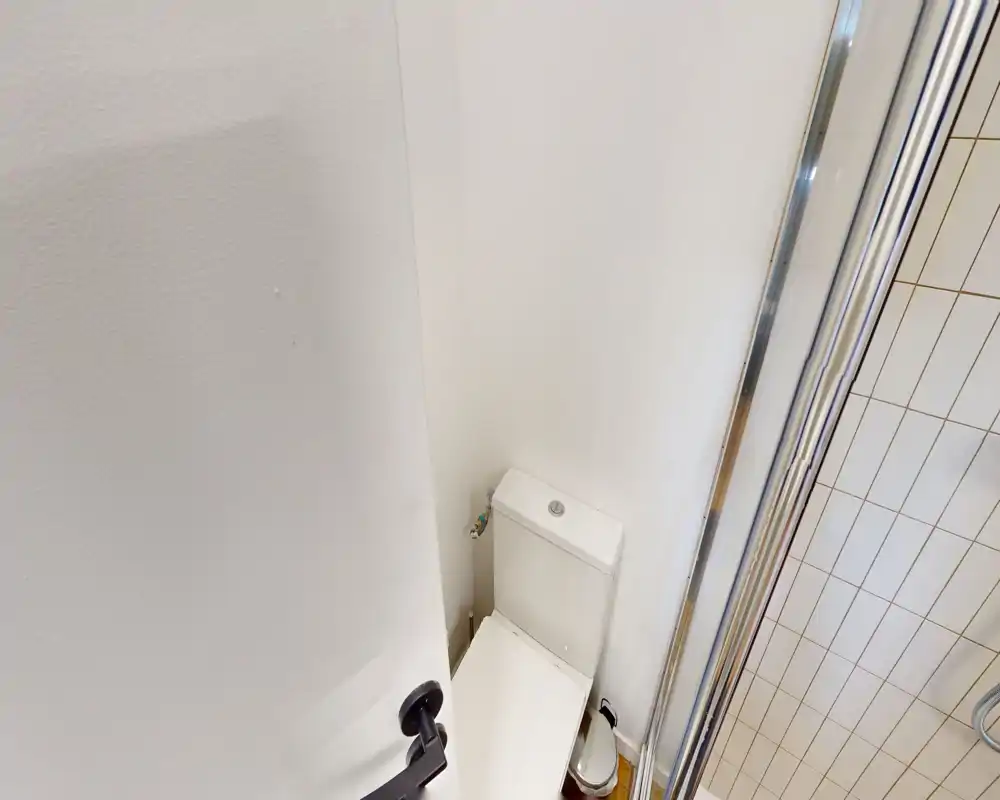 Salle de bains compacte montrant les toilettes à côté d'une douche carrelée ; espace propre, lumineux et pratique, adapté à une location compacte.
