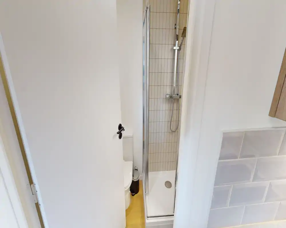 Salle de bain moderne et compacte avec cabine de douche d'angle, douche murale et carrelage. Propre, lumineuse et fonctionnelle, idéale pour les locations courte durée.