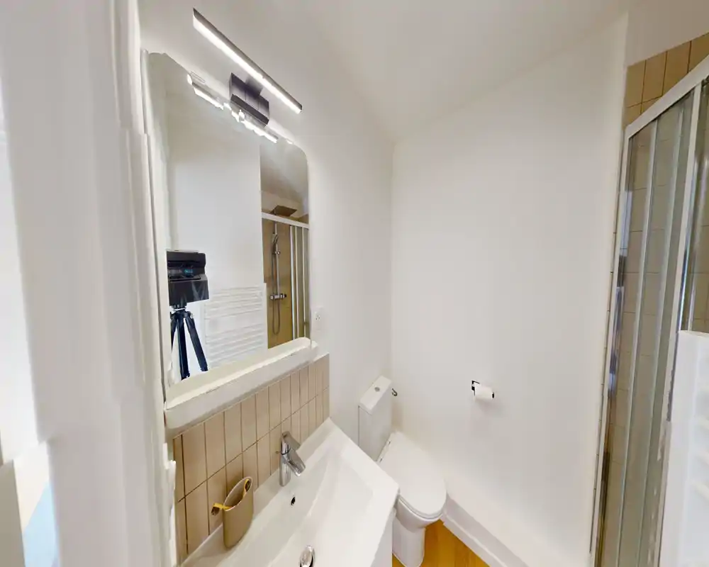 Compact modern bathroom with a sink, mirror, toilet and a glass-enclosed shower. Bright, clean surfaces and neutral tiles create a fresh feel.