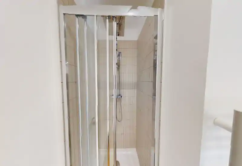 Doccia piastrellata compatta con ante scorrevoli in vetro e doccia cromata a mano — cabina bagno pulita, moderna e ben illuminata.