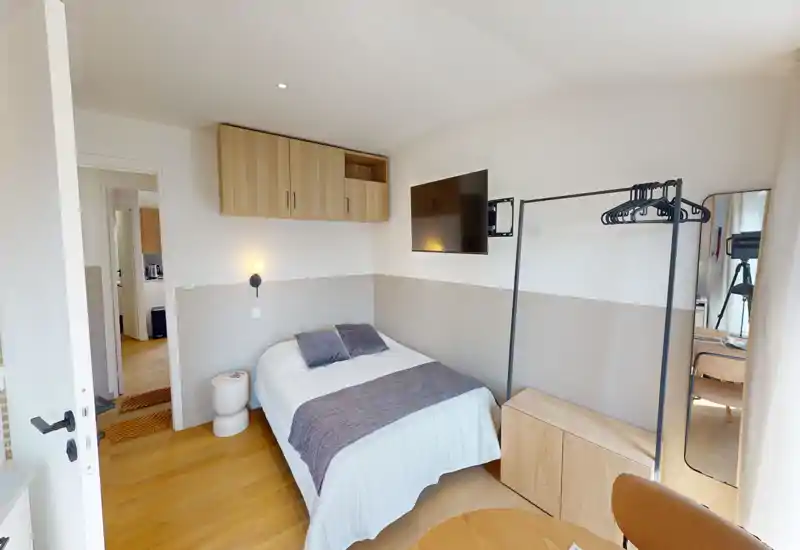 Camera da letto luminosa e ben arredata con letto matrimoniale, TV a parete e contenitori minimal. Pavimento in legno e tessili morbidi creano un'atmosfera accogliente e moderna.