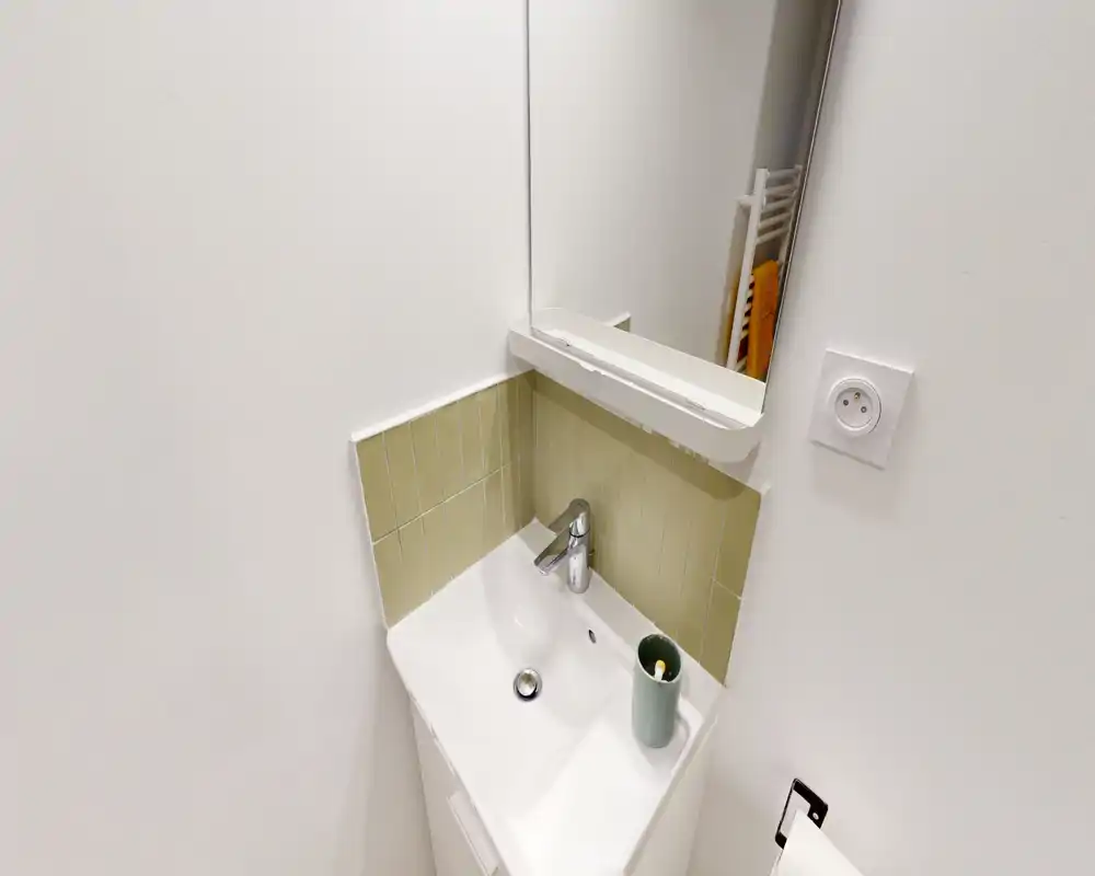 Petit coin lavabo de salle de bain avec robinet moderne, petit miroir et carreaux vert pâle — lumineux, propre et peu encombrant.
