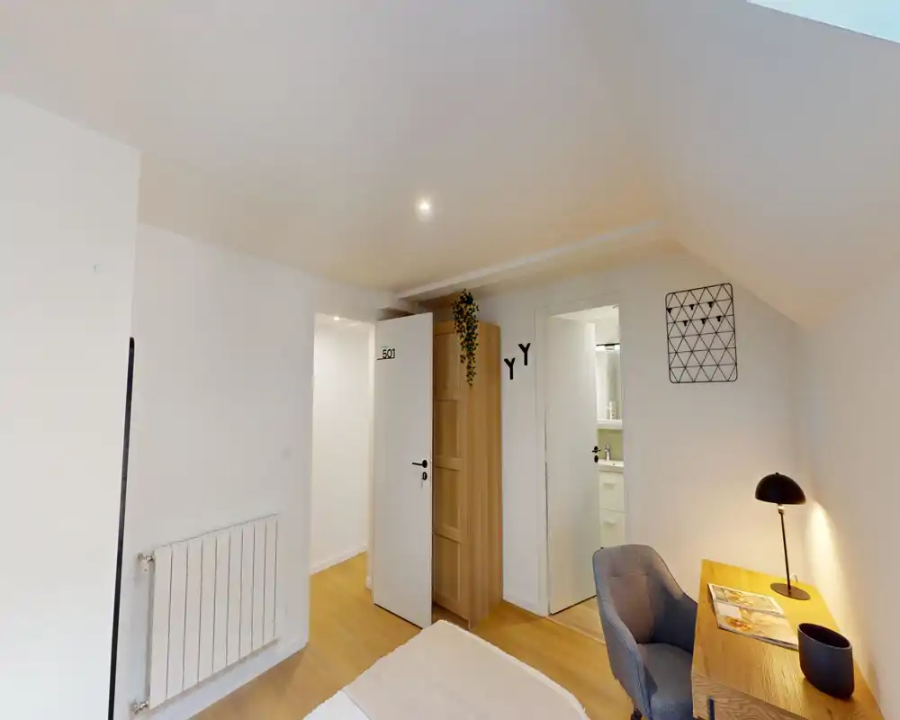 Coin de chambre lumineux et épuré avec lit visible, bureau en bois et fauteuil confortable ; tons neutres et éclairage doux pour une ambiance apaisante.