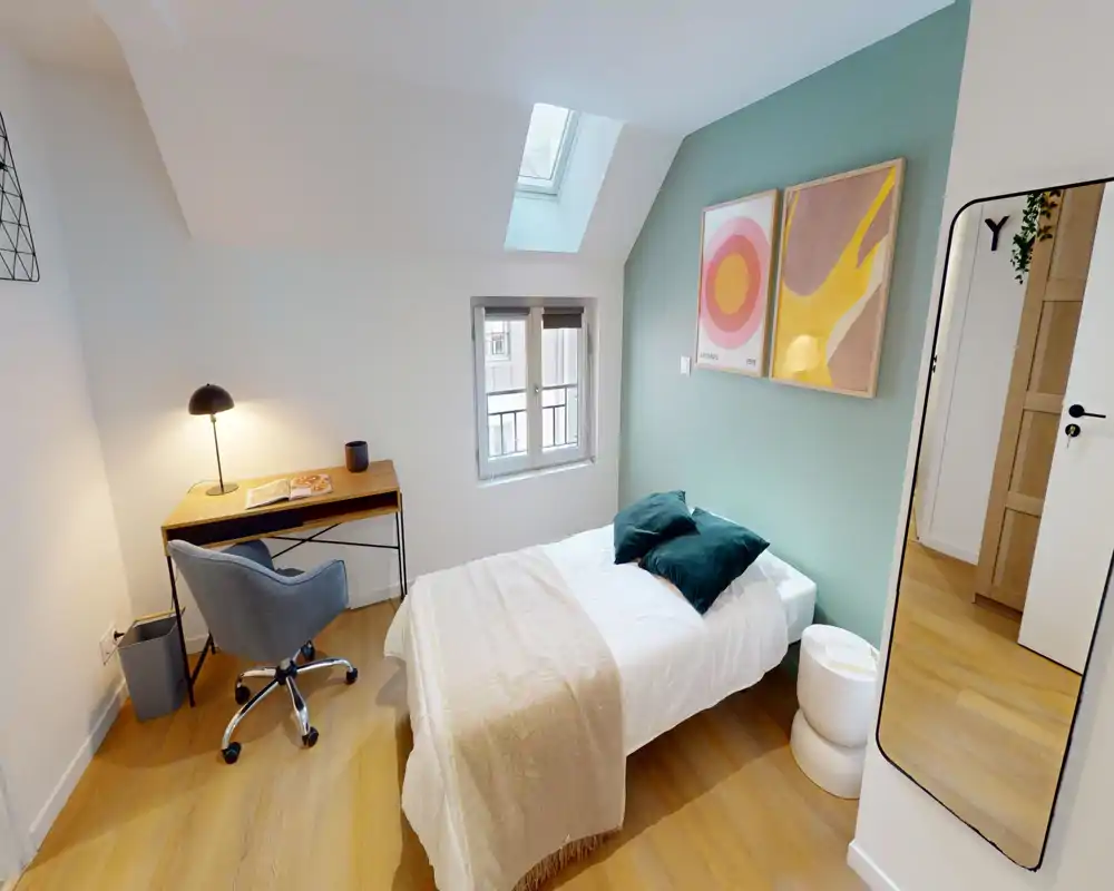 Chambre simple lumineuse et bien décorée avec un lit confortable, un tabouret de chevet et un petit bureau près de la fenêtre; textiles et œuvres murales coordonnés pour une ambiance chaleureuse.