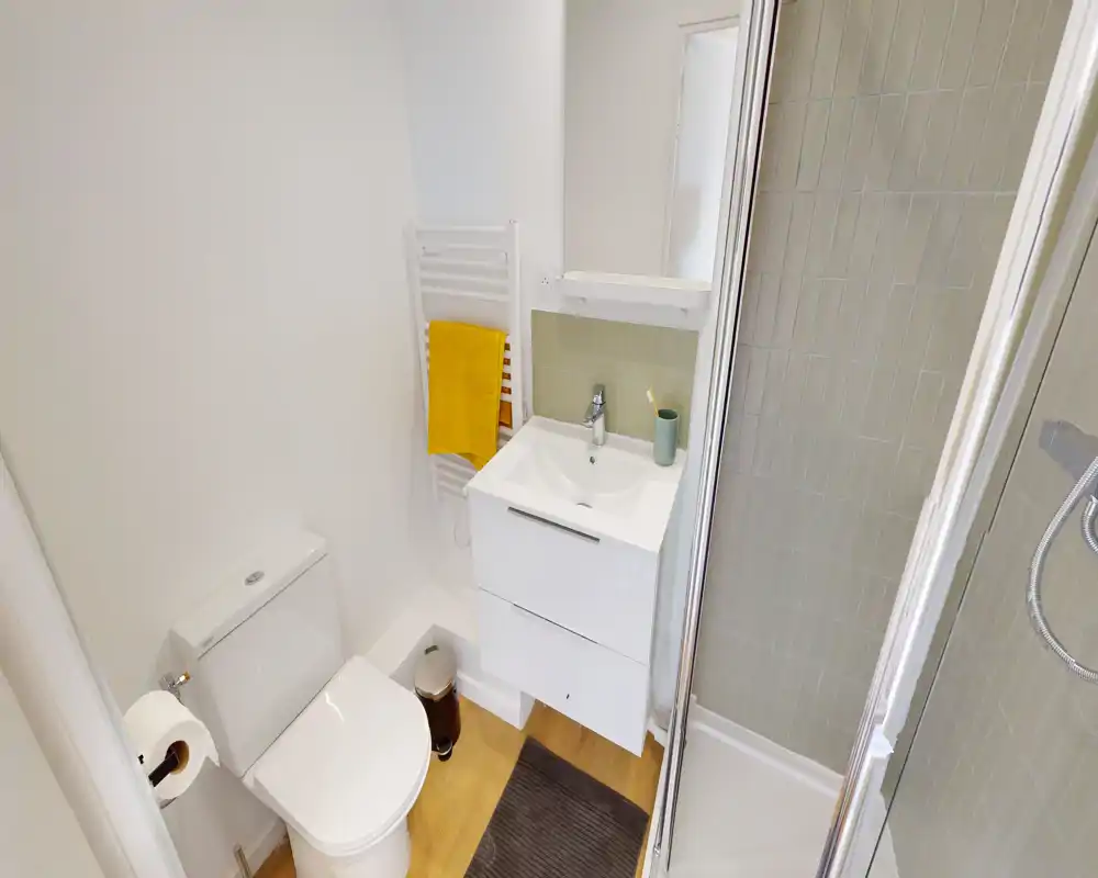 Bagno moderno e compatto con box doccia ad angolo, lavabo con mobile sospeso e wc; pavimento in legno chiaro e scalda-asciugamani.