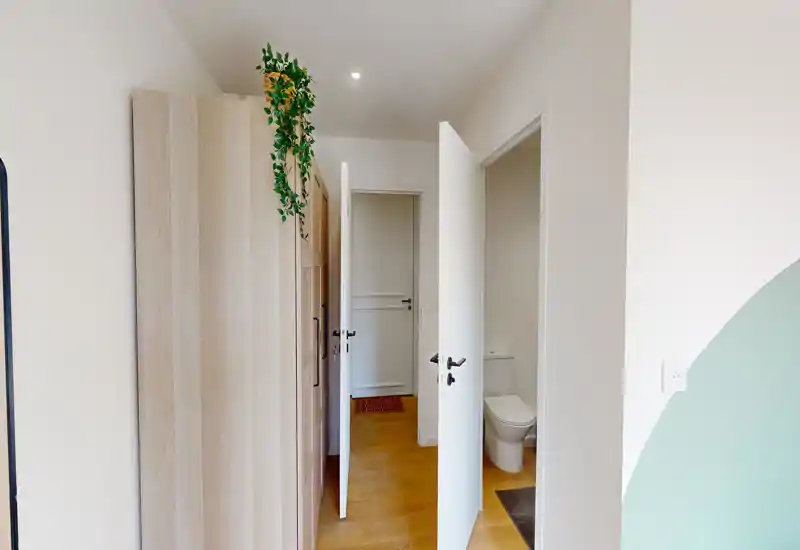 Entrada luminosa con armario empotrado, puertas blancas y suelo de madera; se ve la puerta del baño a la derecha.