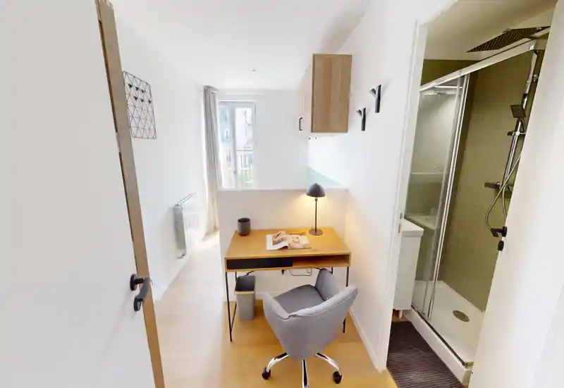 Habitación compacta y luminosa con escritorio de madera, silla giratoria cómoda y ducha en suite; ideal para una persona que busca un estudio con zona de trabajo y buena luz natural.