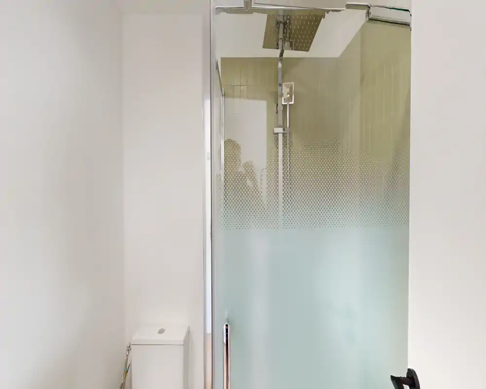 Salle de bains moderne et minimaliste avec douche vitrée et WC compact. Murs blancs et verre dépoli apportent une ambiance lumineuse et contemporaine.