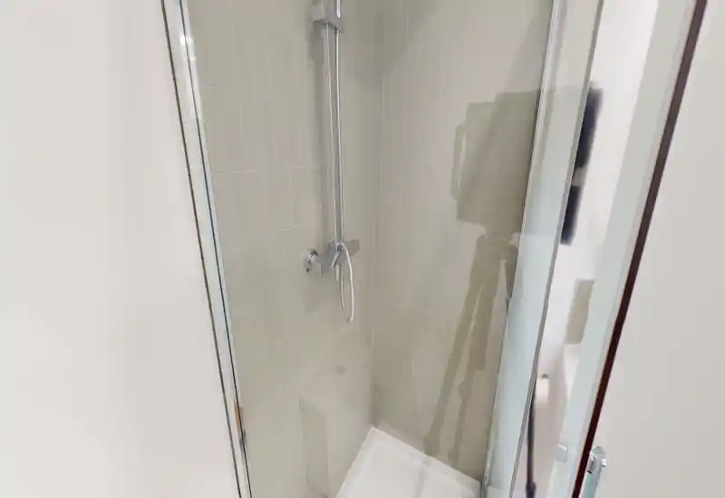 Cabine de douche carrelée compacte avec mitigeur mural chromé et douchette, bac blanc propre et porte vitrée transparente.