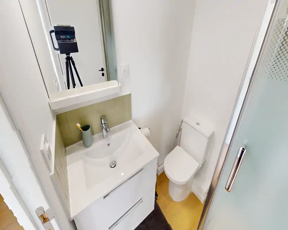 Compact, modern bathroom with a white vanity sink, toilet and a glass shower door; clean, bright and efficiently laid out.