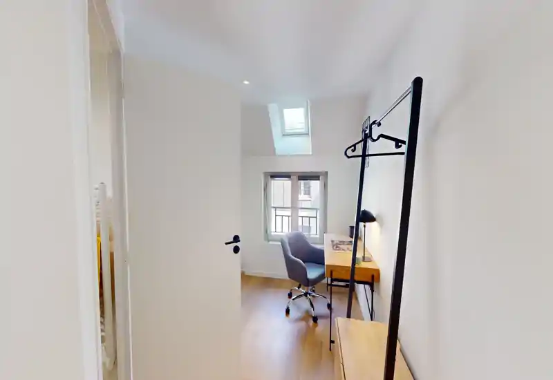 Petite pièce lumineuse avec bureau, chaise et puits de lumière ; peu d’éléments typiques d’une chambre. Idéale pour un espace de travail ou une chambre simple compacte avec lumière naturelle.