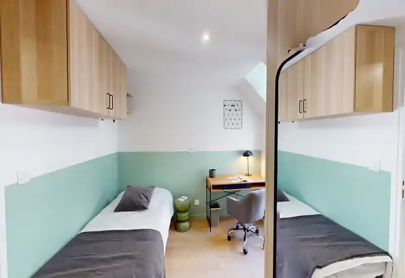 Chambre lumineuse et bien décorée avec lits jumeaux, petit bureau et rangements en bois intégrés — idéale pour étudiant ou séjour court.