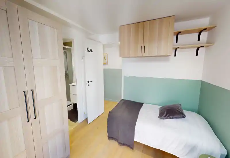 Chambre compacte et soignée avec un lit simple, une armoire en bois et des rangements muraux. Décor lumineux et frais avec une demi-cloison vert menthe et des tons boisés chaleureux.