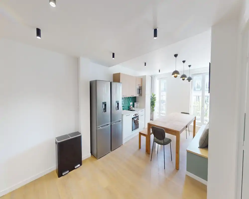 Cucina open space moderna con frigorifero in acciaio, forno integrato e tavolo in legno vicino a grandi finestre illuminate — un ambiente funzionale e ben illuminato ideale per pranzi e convivialità.
