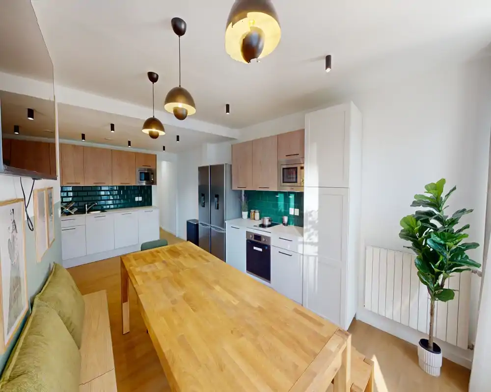 Cucina open-space moderna con tavolo in legno, rivestimento a mattonelle verde, elettrodomestici integrati e panca accogliente — luminosa e ben curata per annunci.