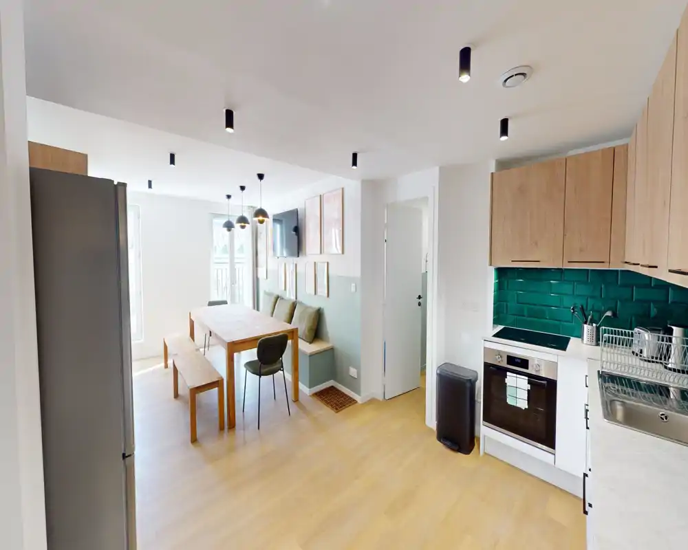 Cucina moderna a vista, luminosa, con pensili in legno, paraschizzi in piastrelle verdi, forno integrato e panca pranzo con cuscini — perfetta per pasti conviviali.