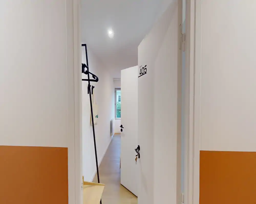 Bright, minimal entrance corridor with an open numbered door (405), wall hooks and a small bench — clean, well-lit access to the apartment.