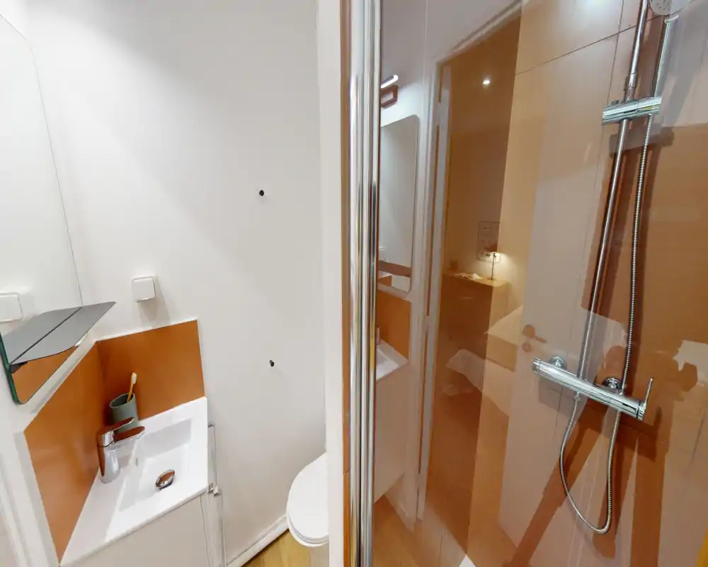 Compact modern bathroom with a walk-in shower, chrome fixtures, a small sink with mirror and a wall-mounted toilet. Warm-toned tiles and wood-look flooring create a cozy feel.