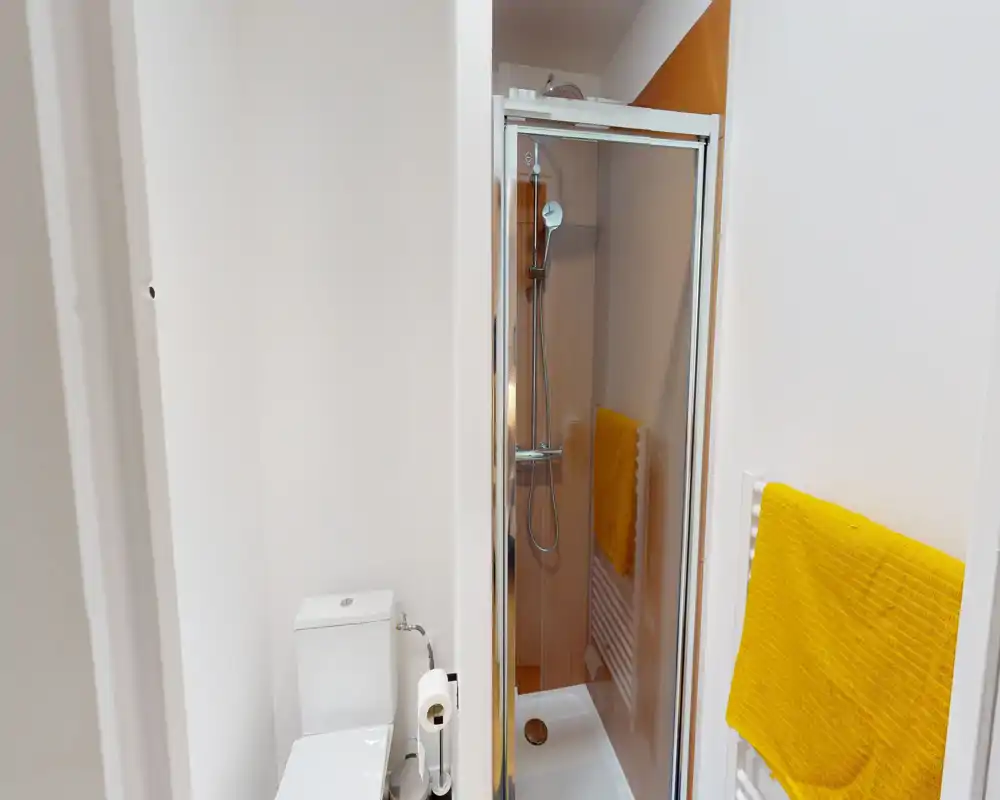 Compact modern bathroom with a shower cabin, toilet and bright yellow towels; clean white walls and good natural lighting.