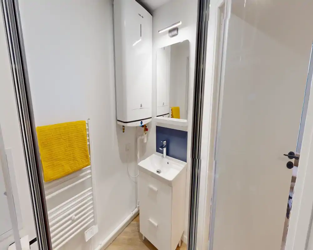 Compact modern bathroom with a small vanity sink, wall-mounted mirror and a heated towel rail with a bright yellow towel; clean, well-lit and recently renovated look.
