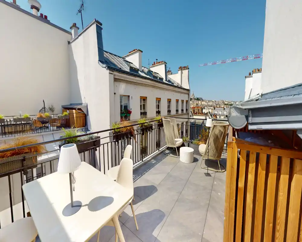 Sunny private terrace with outdoor seating and city views, featuring a dining table, lounge chairs and planters — ideal for relaxing or dining al fresco.