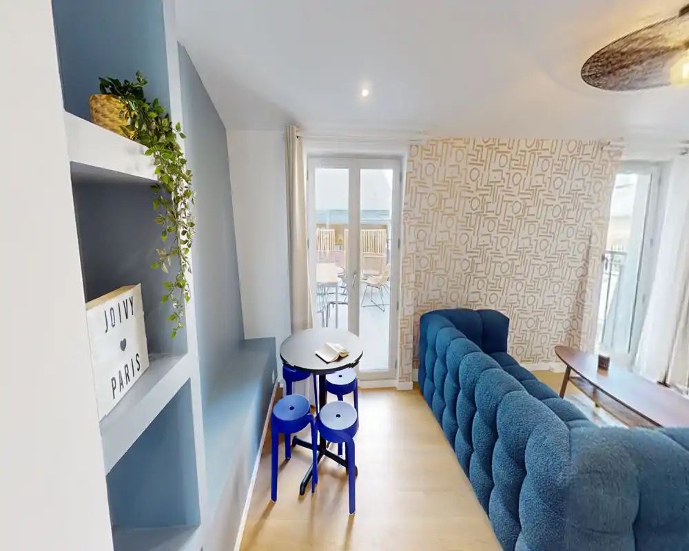 Bright, stylish living room with a deep blue tufted sofa, patterned accent wall and glass doors opening to a balcony — comfortable seating and tasteful decor.