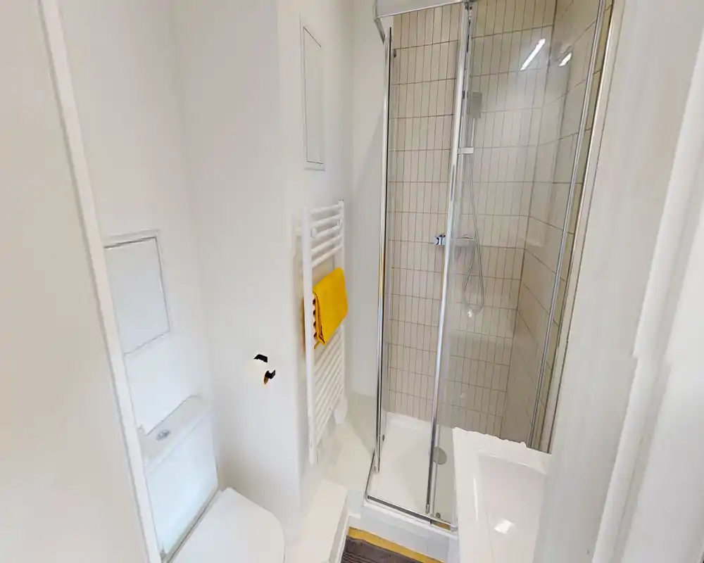 Bagno compatto e moderno con doccia delimitata da vetro, piastrelle bianche e scalda-asciugamani con asciugamano giallo.