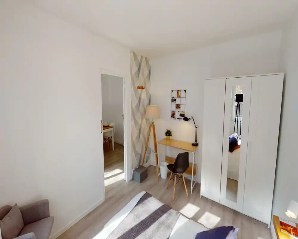 Camera da letto moderna e luminosa con letto comodo, armadio con anta a specchio e una piccola scrivania con lampada a treppiede — perfetta per una persona o coppia che cerca una stanza ordinata e soleggiata.