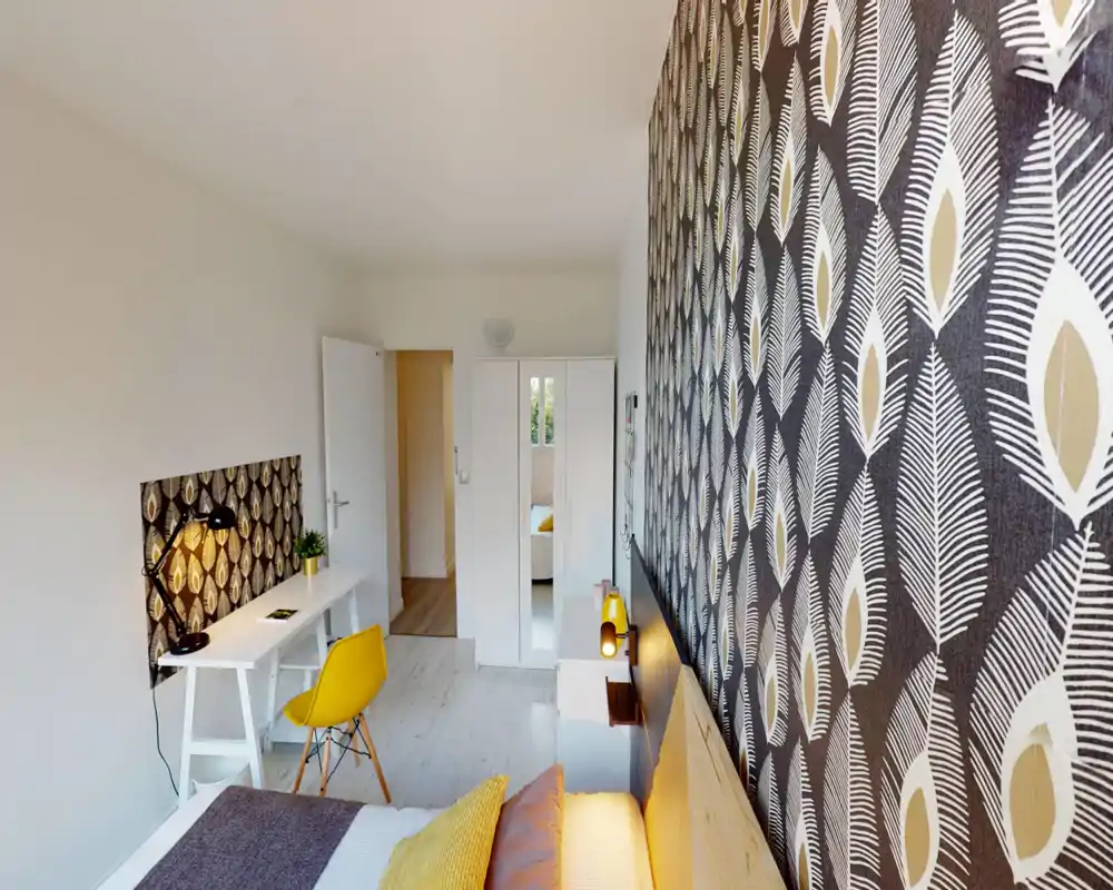 Bright, modern bedroom with patterned feature wall, cozy bed with cushions and a functional desk area. The room feels fresh and well styled, with warm accents and good natural light.