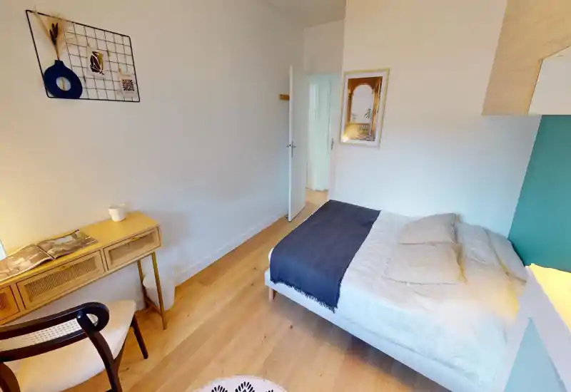 Chambre simple lumineuse et bien mise en scène avec un lit confortable, un bureau d'appoint et un parquet chaleureux — idéale pour une annonce locative mettant en avant le confort et la décoration soignée.