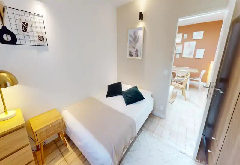 Chambre compacte et décorée avec soin, lit double en linge neutre, deux coussins décoratifs et une lampe de chevet chaleureuse — ambiance cosy, idéale pour un voyageur seul ou un couple.