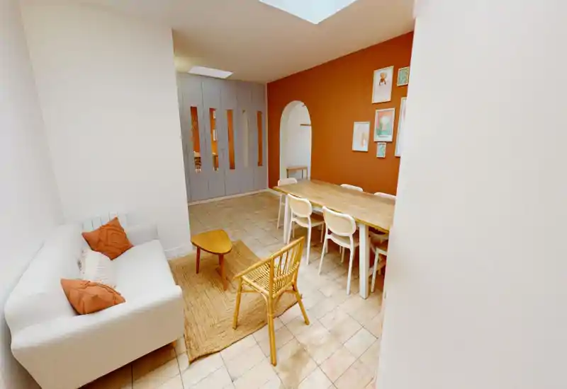 Espace séjour et salle à manger lumineux et stylé avec canapé confortable, tapis en fibres naturelles et grande table en bois devant un mur d'accent terracotta chaleureux.