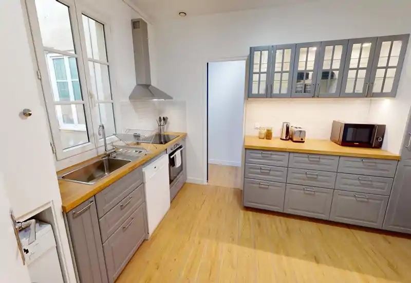 Bright modern kitchen with gray cabinetry, wooden countertops and integrated appliances. Large window provides natural light and the layout offers ample storage and workspace.