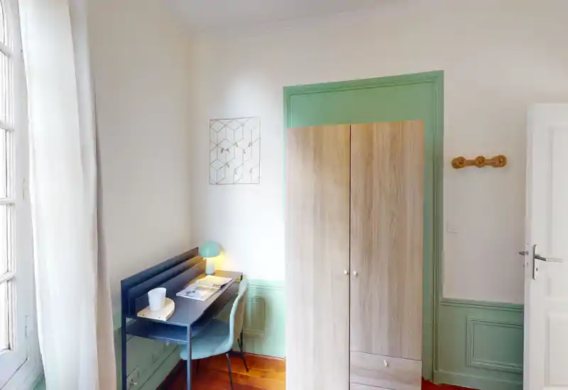 Bright, tidy bedroom corner with a wardrobe, small desk and chair near a large window — ideal for work or light storage.
