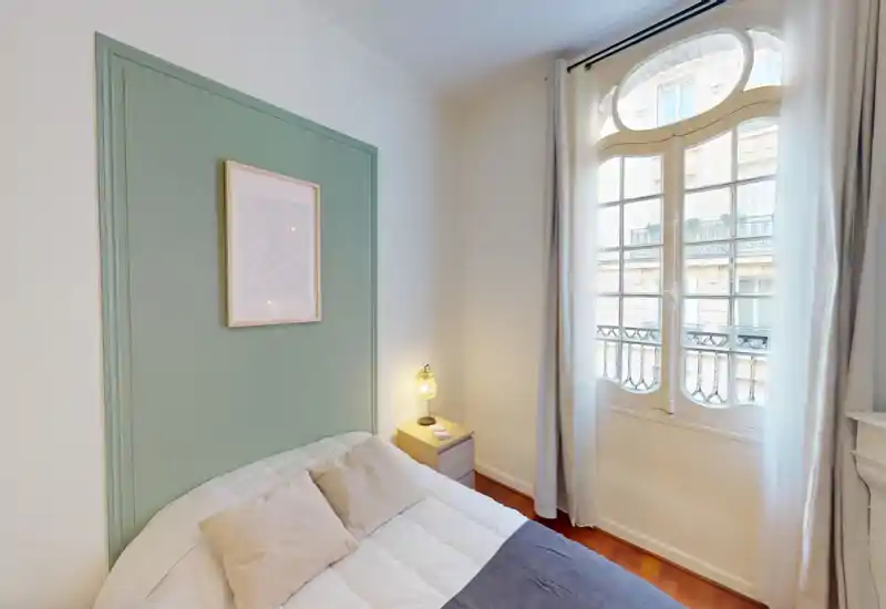 Camera da letto luminosa e accogliente con un comodo letto matrimoniale, comodino e una grande finestra decorativa che permette molta luce naturale.