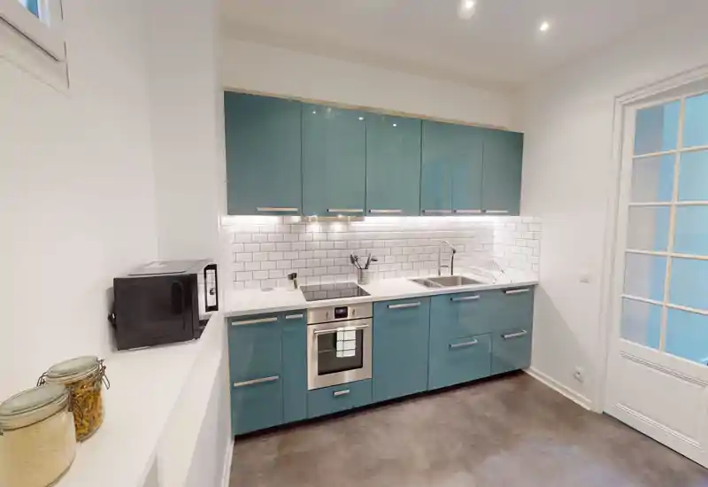 Cuisine moderne et lumineuse avec meubles bleu-vert, four encastré, évier et crédence en carreaux métro; présentation soignée et éclairage sous les meubles, idéale pour une annonce d'appartement.