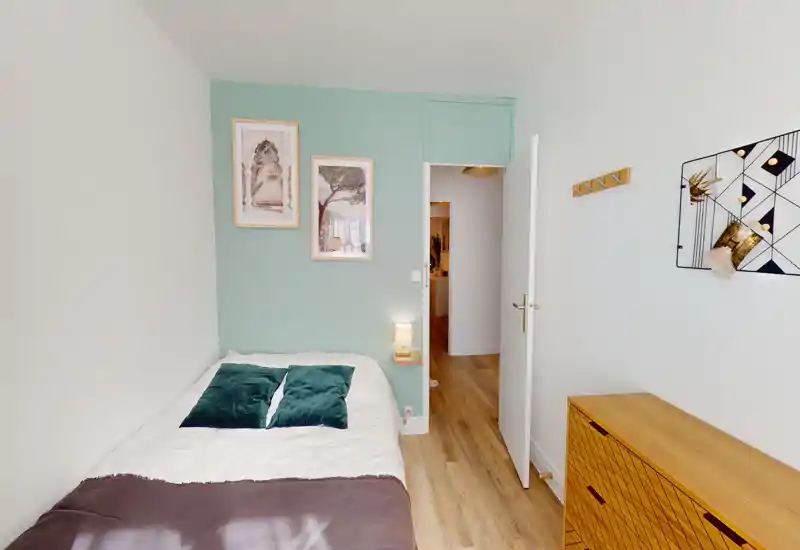 Bright, well-styled single bedroom with a comfortable bed, green accent wall, bedside lamp and wooden storage cabinet — ideal for a cozy rental stay.